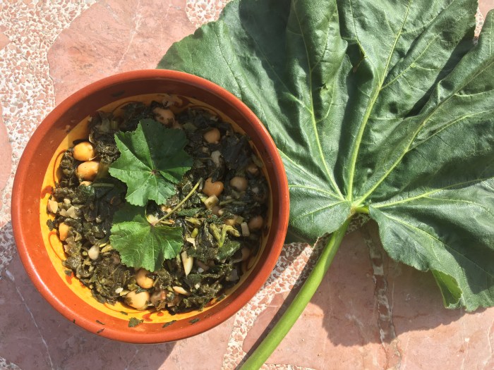 Picture of cooked mallow leaf with chickpeas in a bowl, with a large mallow leaf on the side